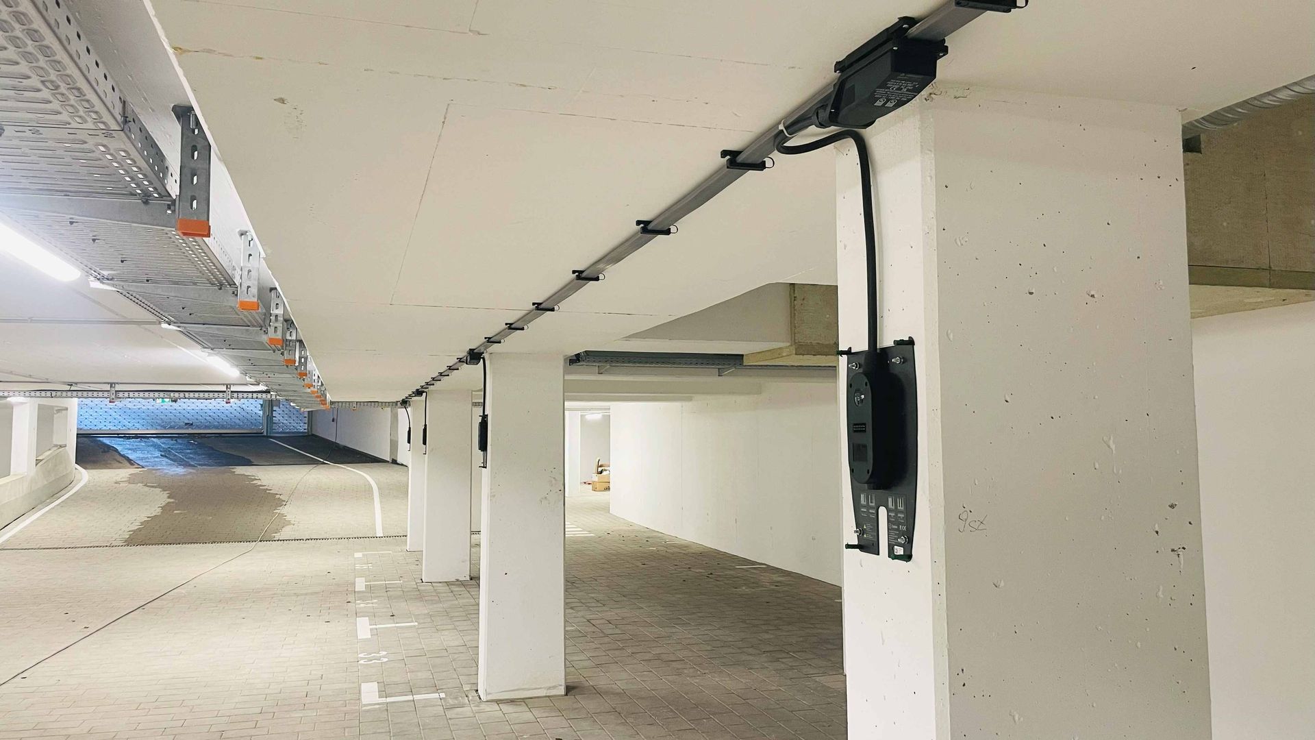 Installation im Prozess. Dieses Foto bildet eine Tiefgarage ab, in der an der Decke die Stromleitungen laufen, die Ihr Auto laden werden. Dieses Foto ist aus dem Prozess der Installation, noch hängen hier nur die Rückplatten