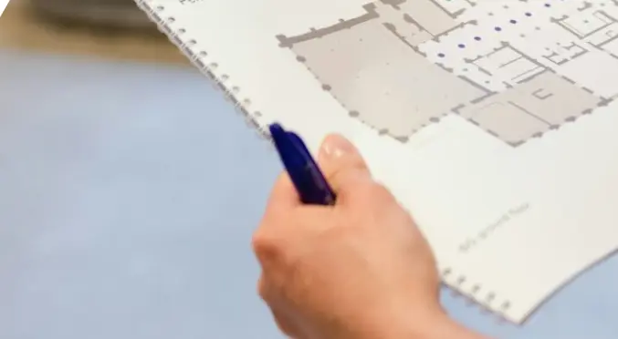 Eine Hand hält die ingenieurs-bauzeichnung eines Grundrisses, in dem Ladepunkte und Infrastruktur verzeichnet werden