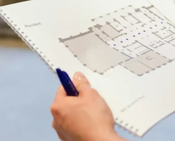 Eine Hand hält die ingenieurs-bauzeichnung eines Grundrisses, in dem Ladepunkte und Infrastruktur verzeichnet werden